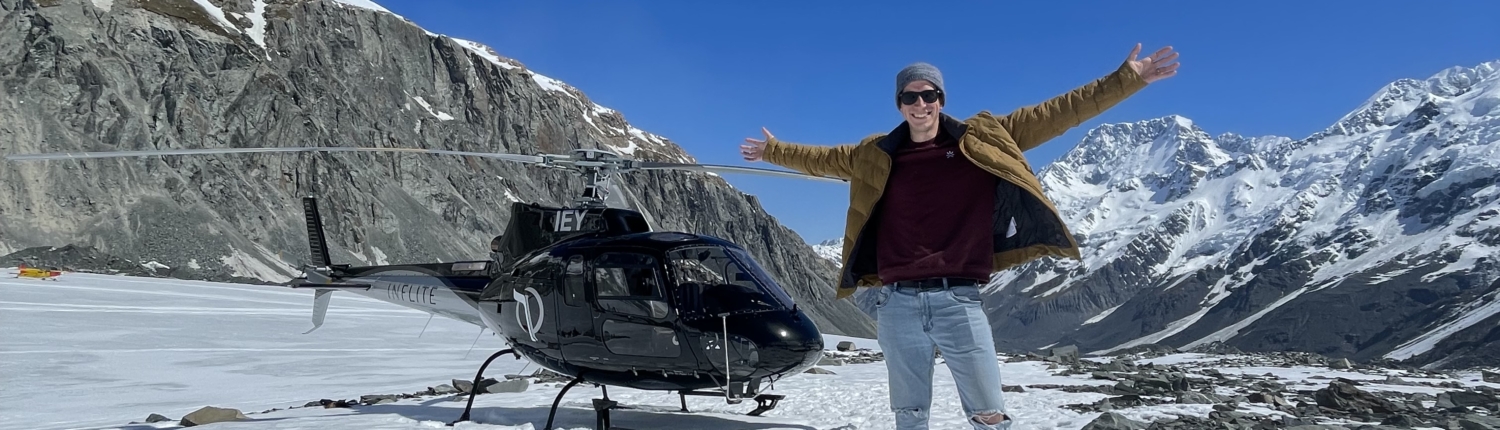 Tourist stands arms open in front of Inflite Helicopter on Tasman Glacier in Mountains