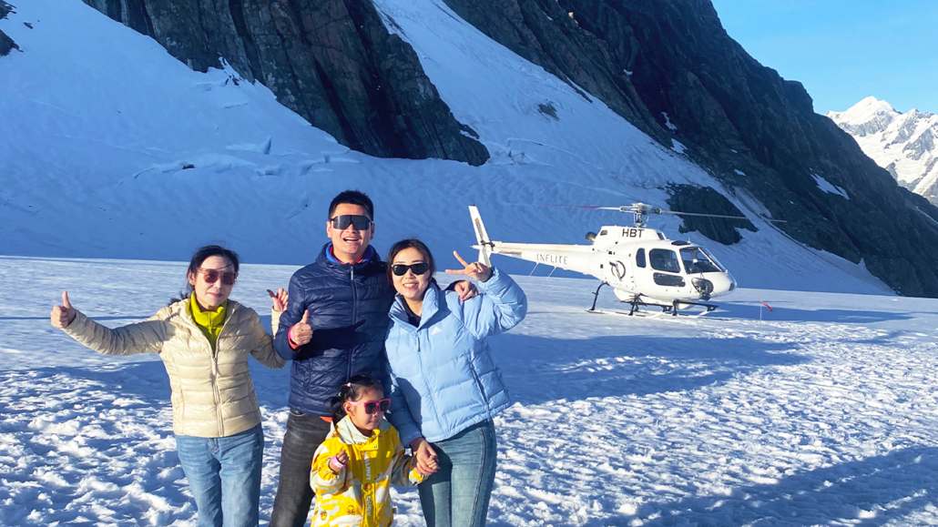 Happy tourists pose for photo on Tasman Glacier infornt of Inflite Helicopter